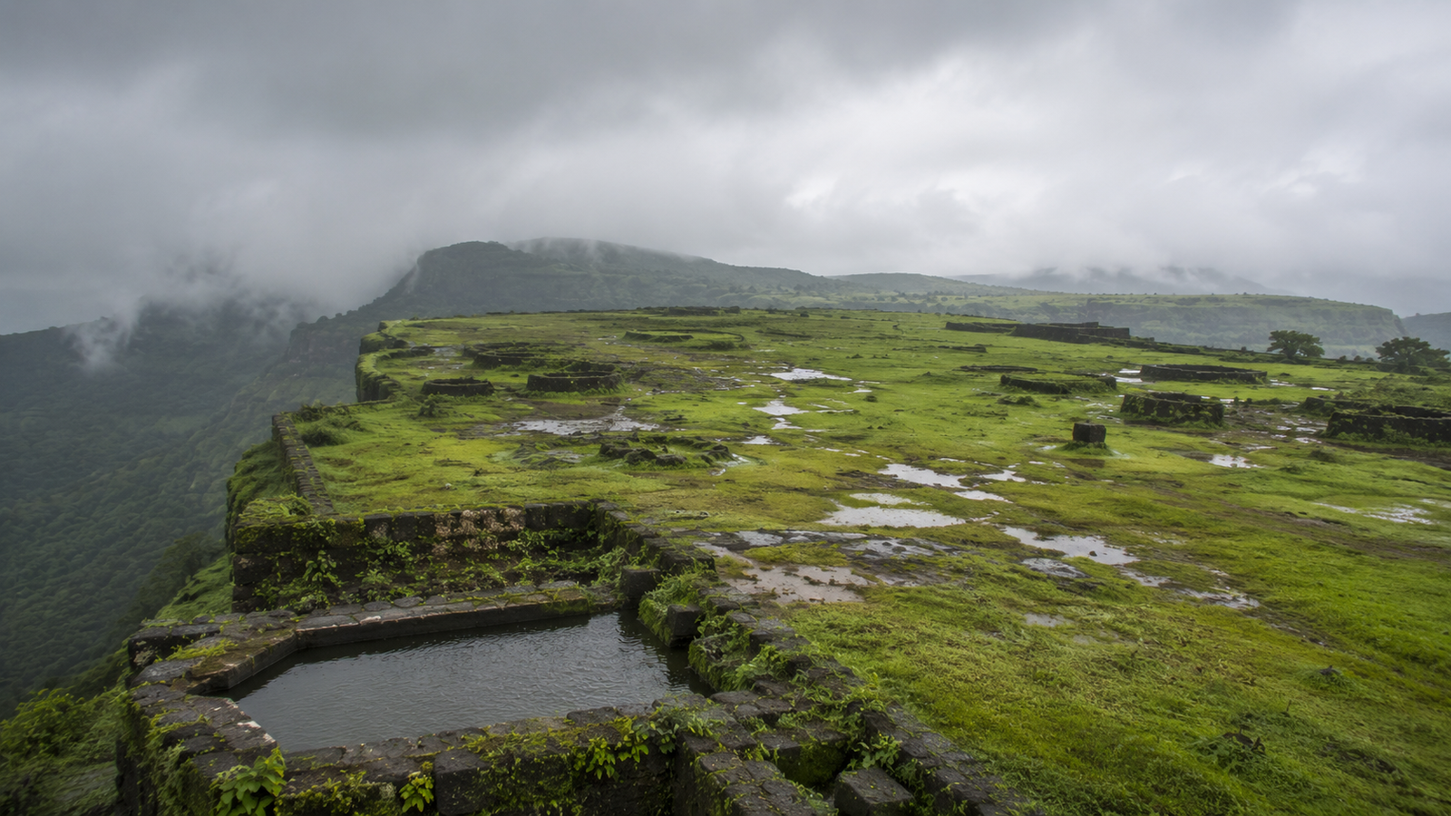 The broad empty plateau of Visapur Fort with old stone water cisterns