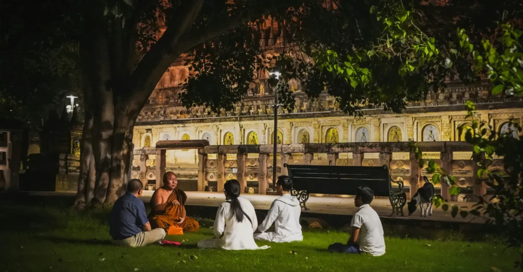 The Mahabodhi Temple lit at dusk with visitors resting on the lawn, Bodh Gaya, Bihar
