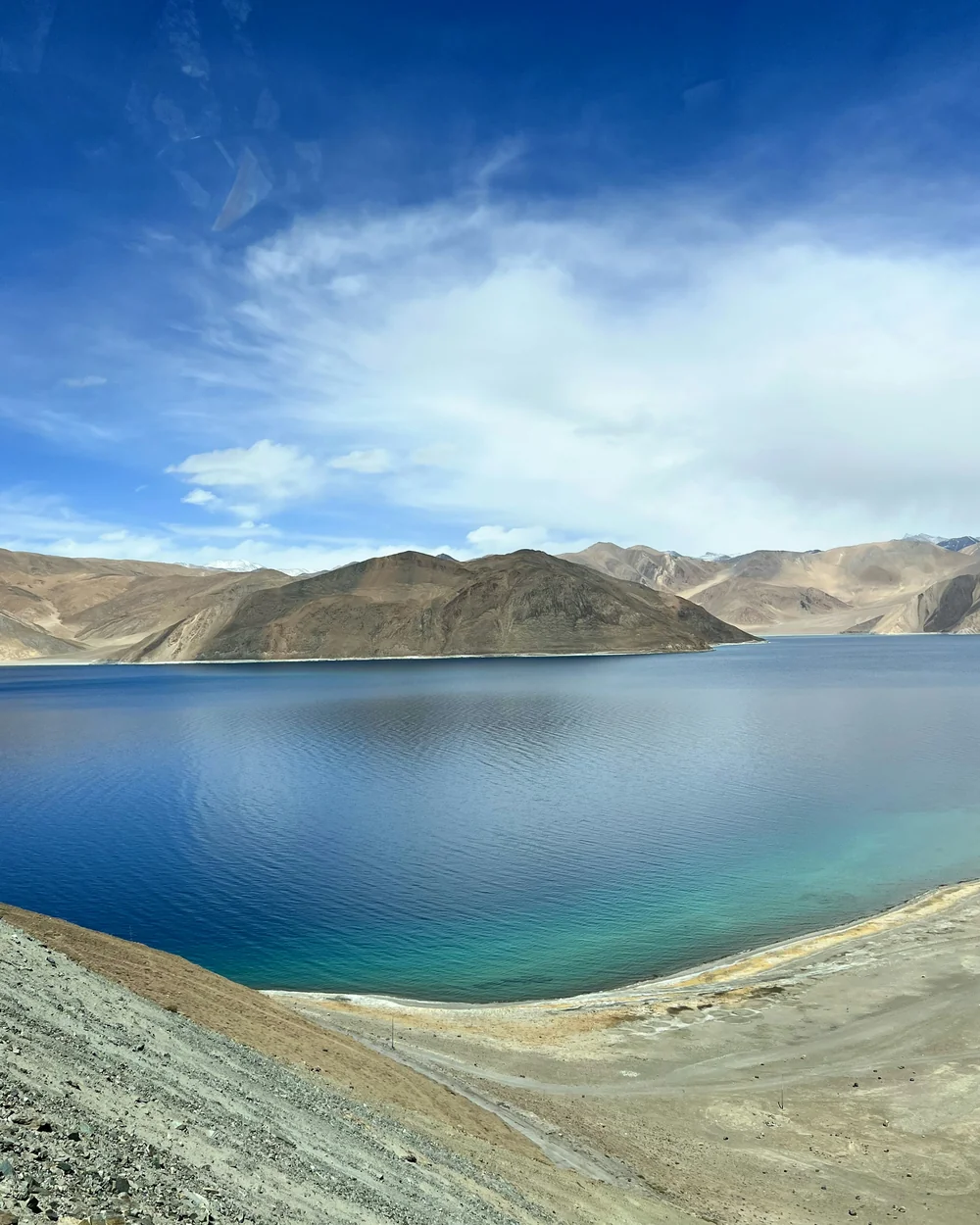 The deep blue water of Pangong Tso curving past a pale sand spit, with bare Ladakhi ranges behind