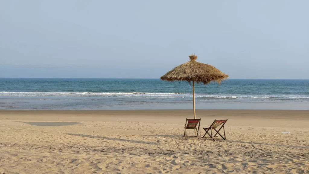 A quiet beach with a thatched umbrella and empty chairs at Gopalpur-on-Sea, Odisha