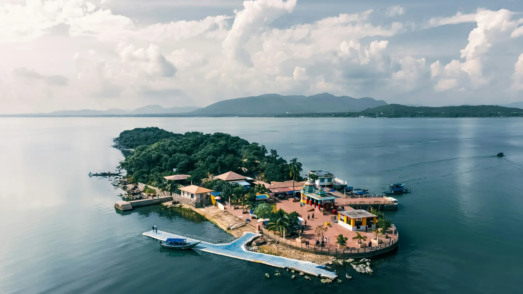 An aerial view of the small wooded Kalijai temple island in Chilika Lake with hills beyond