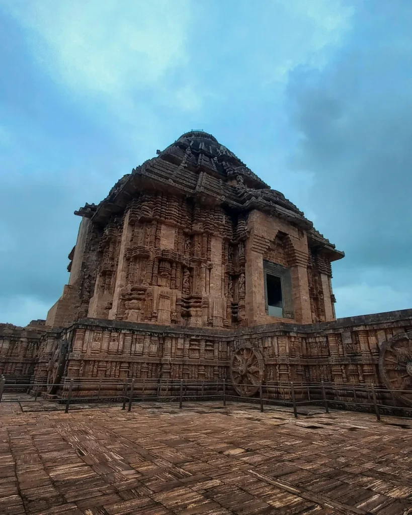 The carved stone jagamohana of the Konark Sun Temple rising against a cloudy sky, with chariot wheels along its base