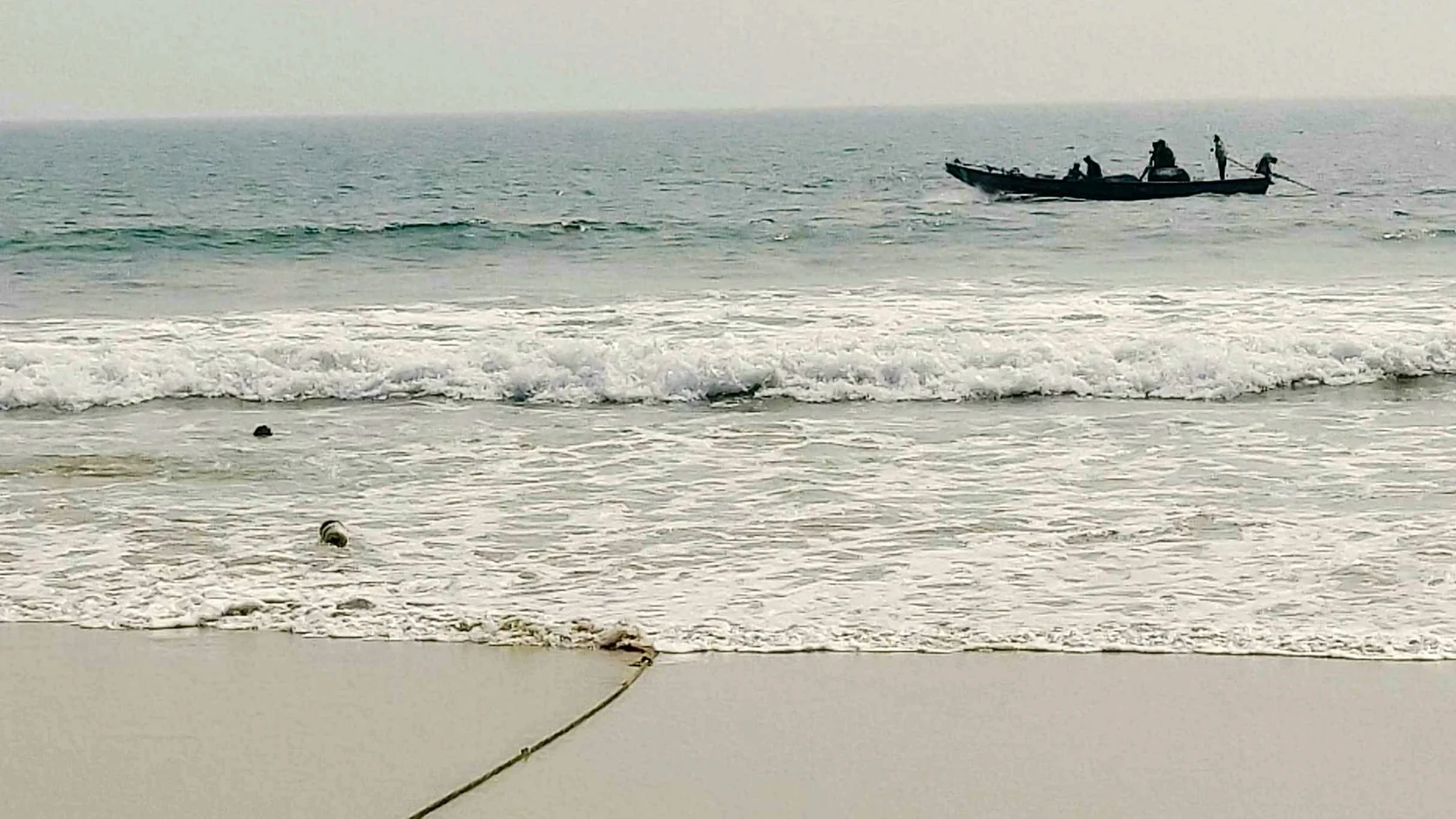 A wooden fishing boat offshore at Puri Beach with a mooring rope running up the empty sand