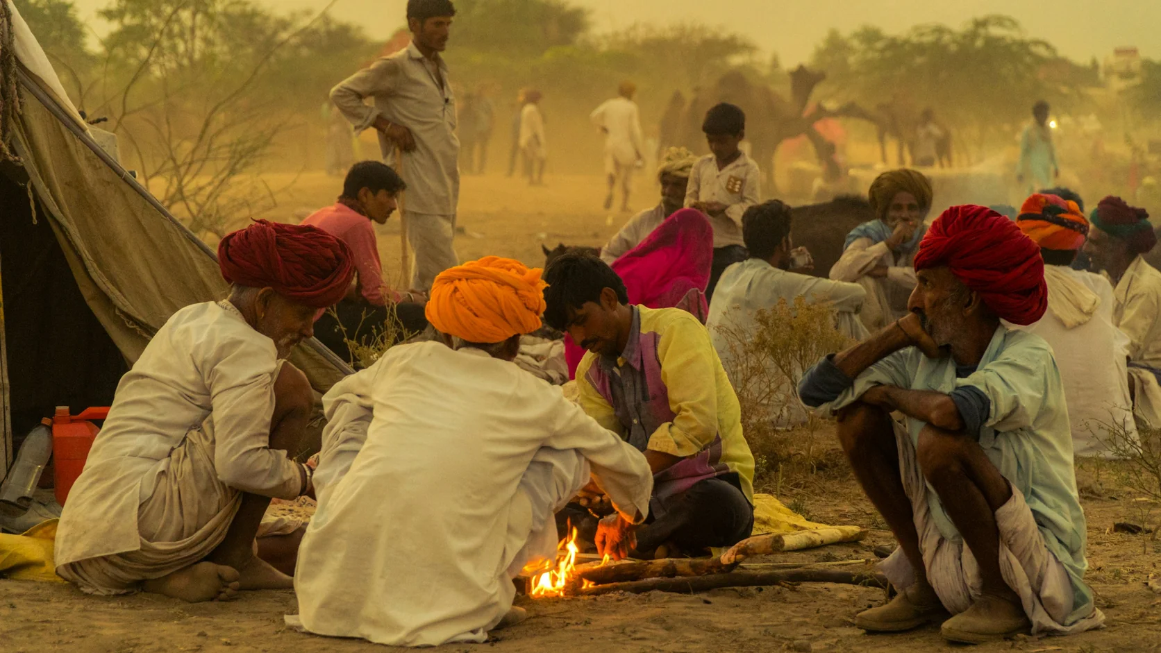 Rajasthani herders in bright turbans sitting around a small fire beside a tent at dawn on the Pushkar fairground