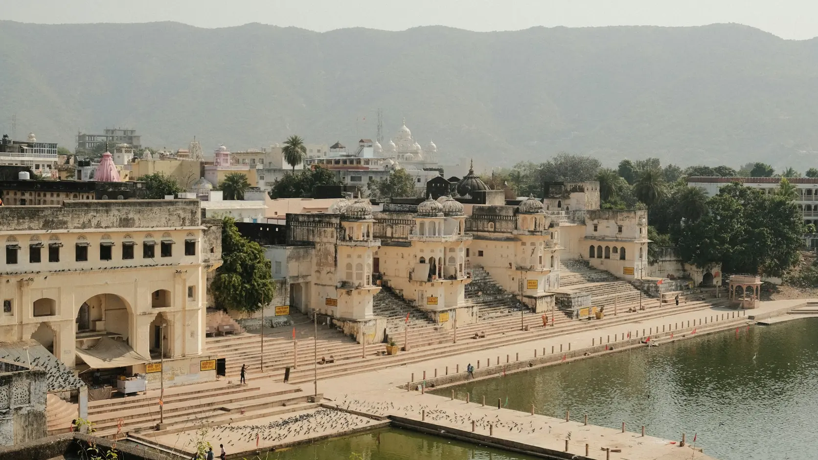 Pushkar Lake with stepped ghats and pale temple buildings along the water, the Aravalli hills behind
